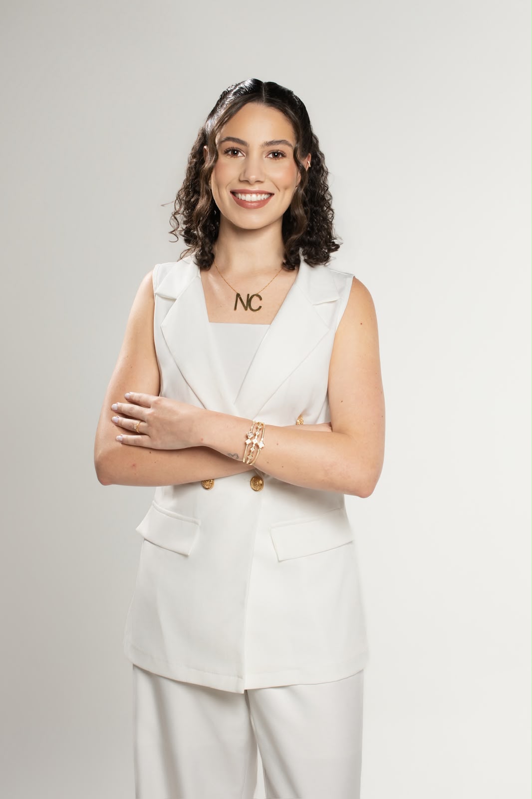 Dra. Nathália Cardoso de conjunto branco, braços cruzados e sorrindo, em fundo claro